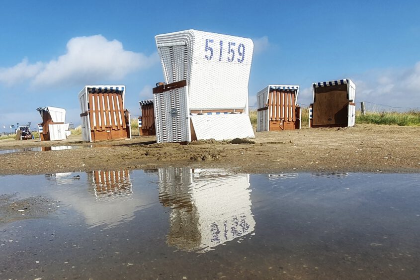 Landschaftsfotografie in Dithmarschen: Ein weißer Strandkorb mit der Nummer 5158 auf sandigem Boden an der Nordseeküste bei Marne im Sommer.