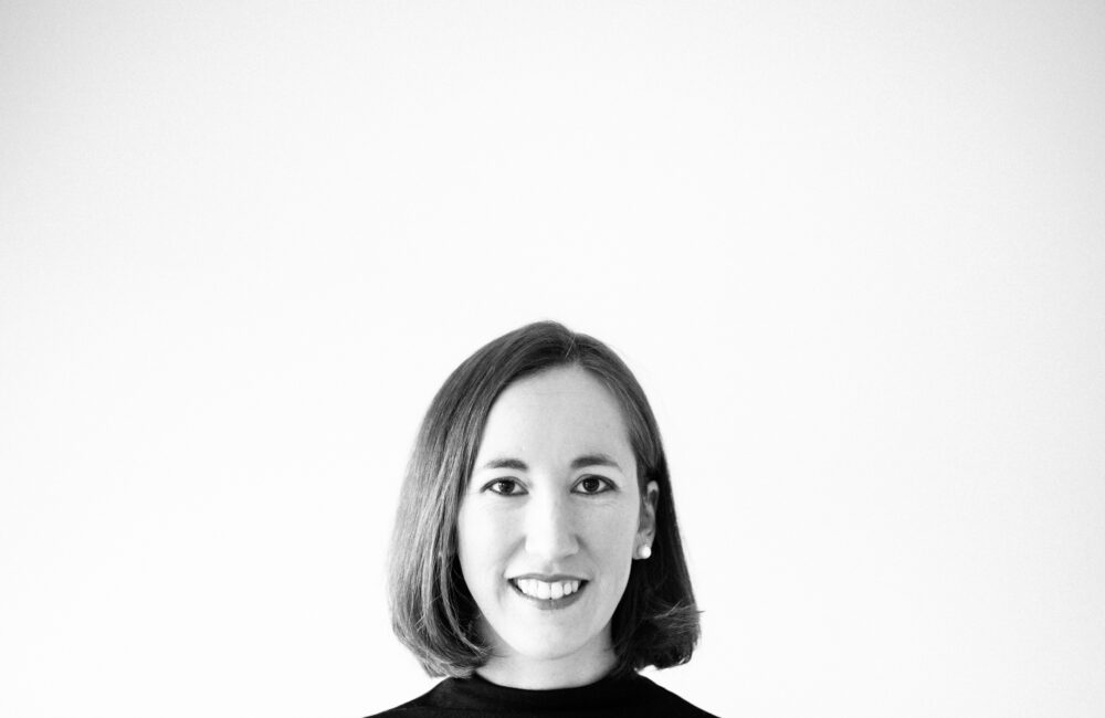 Künstlerische Business-Portraits: Schwarz-weißes, minimalistisches Charakter-Portrait einer lächelnden Frau vor weißem Hintergrund mit viel freiem Raum im oberen Drittel.