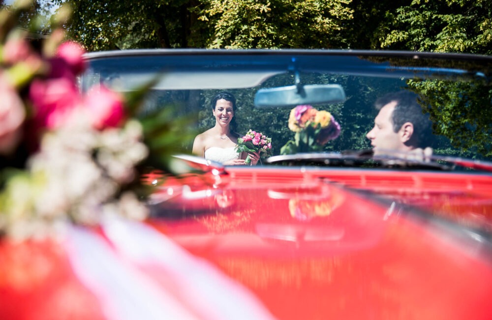 Künstlerische Hochzeitsfotografie in Berlin: Braut spiegelt sich im roten Hochzeitsauto, fotografiert von Hochzeitsfotograf aus Stuttgart / Heilbronn.