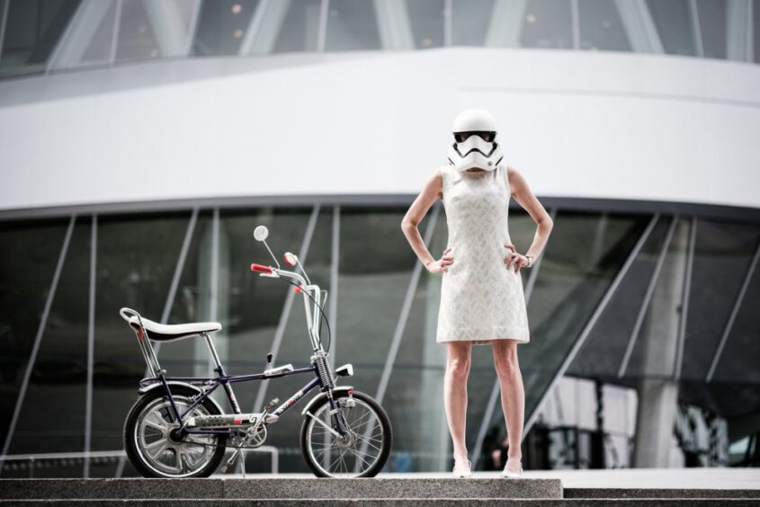 Künstlerische Portraits: Eine Frau im weißen Kleid steht neben einem Bonanza Rad und einem Stormtrooper, überregionaler Portraitfotograf.