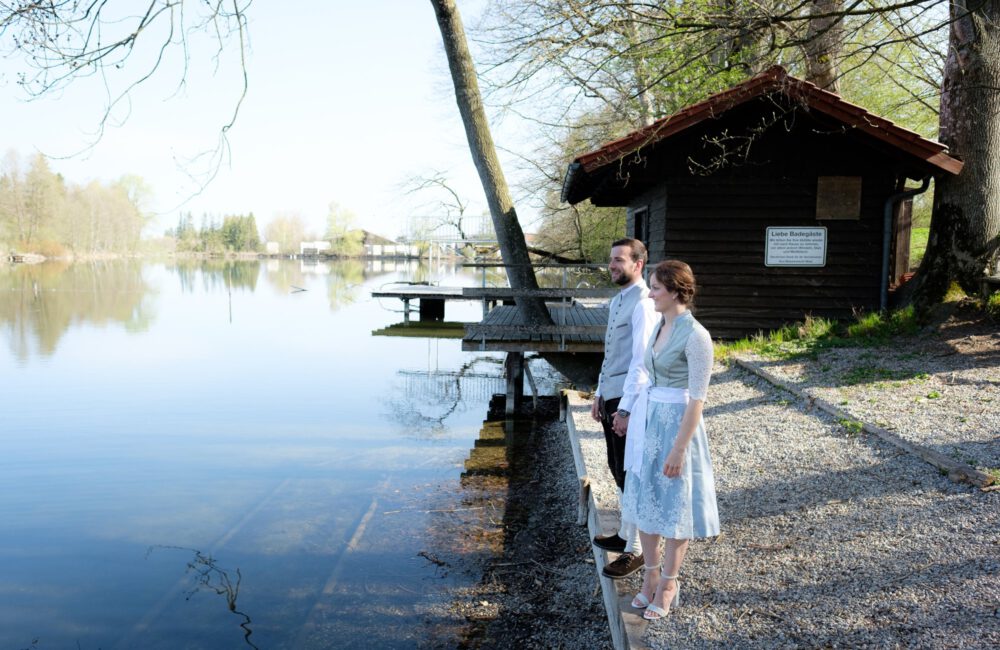 Blick über den Dießener Weiher bei Waal, das Brautpaar klein am Ufer – Hochzeitsfotograf Allgäu