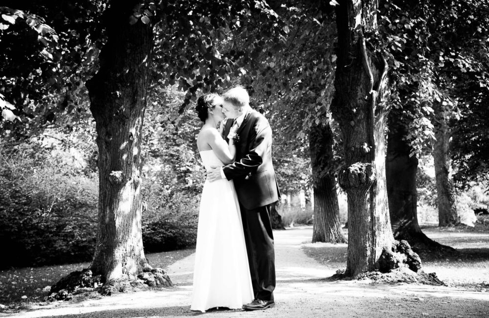Brautpaar küsst sich unter einer Baumallee im Schlossgarten Glienicke, Schwarzweiß — Hochzeitsfotografie Berlin
