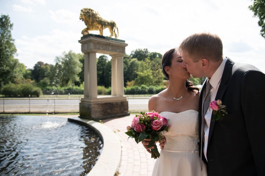 Sarah und Timo küssen sich im Brautkleid vor derselben Löwenfontäne wie vier Wochen zuvor.
