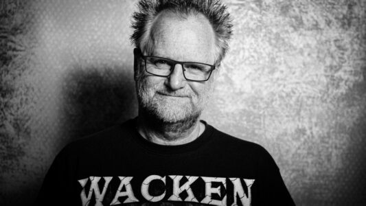 Peter Gödecke im Wacken-Shirt, Schwarzweiß-Selbstporträt vor rauer Wand – Charakter-Fotograf aus dem Raum Heilbronn