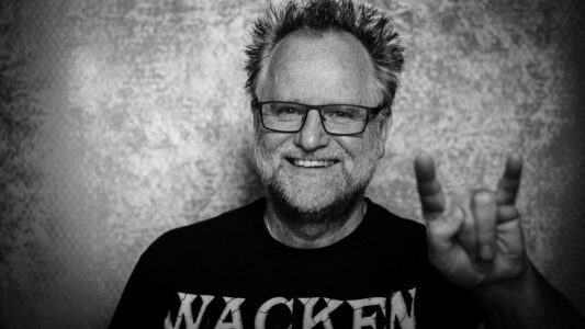 Peter Gödecke zeigt die Metal-Hörner im Wacken-Shirt, Schwarzweiß-Selbstporträt eines Konzertfotografen
