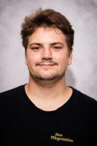 Junger Mitarbeiter der Pflegestation im Portrait vor grauem Hintergrund – Portraitfotografie für Pflegedienste, Fotograf Heilbronn