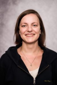 Mitarbeiterin der Pflegestation im Portrait, freundlich lächelnd vor grauem Hintergrund – Portraitfotografie für Pflegedienste, Fotograf Heilbronn