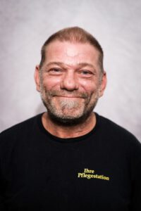 Bärtiger Mitarbeiter der Pflegestation im Portrait vor grauem Hintergrund – Portraitfotografie für Pflegedienste, Fotograf Heilbronn