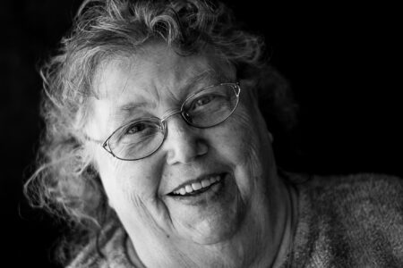 Schwarz-weiß-Portrait einer fröhlich lachenden Seniorin mit Brille und Locken im Fensterlicht – Projekt Lebensspuren, Fotograf Heilbronn-Allgäu-Hamburg-Bremen