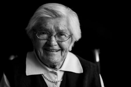 Schwarz-weiß-Portrait einer lächelnden Seniorin mit Brille im Fensterlicht – Projekt Lebensspuren, Fotograf Heilbronn-Allgäu-Hamburg-Bremen