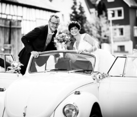 Brautpaar im weißen Käfer-Cabrio mit Blumenschmuck auf dem Weg zur Feier in Hößlinsülz