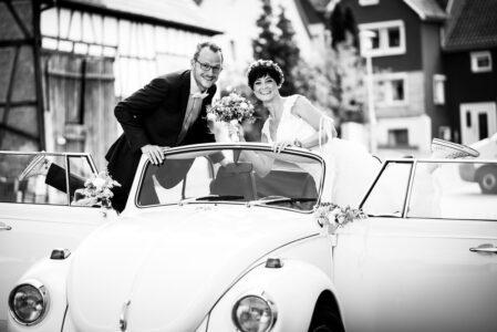 Brautpaar im weißen Käfer-Cabrio mit Blumenschmuck auf dem Weg zur Feier in Hößlinsülz