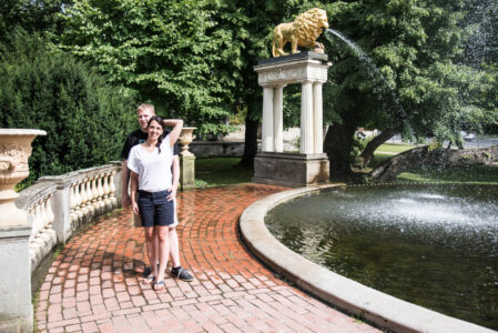 Engagement-Shooting im Schlosspark Klein-Glienicke: Sarah und Timo in T-Shirt und kurzer Hose vor der Löwenfontäne.