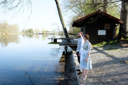 Blick über den Dießener Weiher bei Waal, das Brautpaar klein am Ufer – Hochzeitsfotograf Allgäu