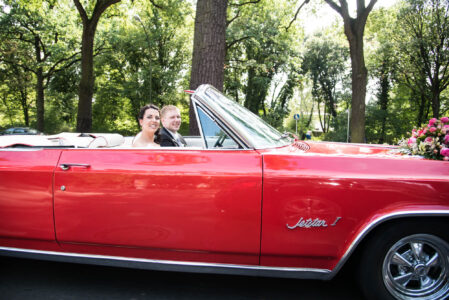 Rotes Oldsmobile-Cabrio als Hochzeitsauto, Blumenschmuck auf der Motorhaube.