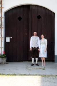 Das Brautpaar klein vor dem großen Holztor des Rathauses Waal – Hochzeit im Allgäu