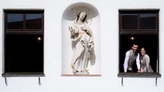 Das Brautpaar im Fenster des Rathauses Waal, daneben eine Madonna in der Mauernische – Hochzeit im Allgäu